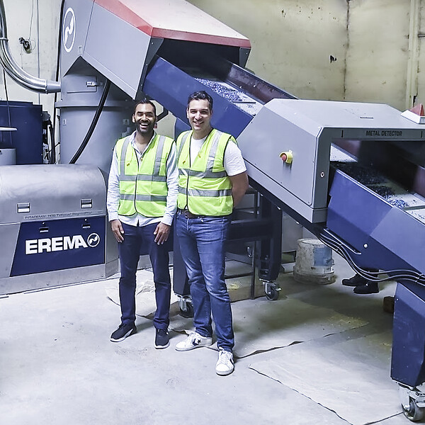 Keiran Smith and Karim Debabe in front of the INTAREMA® 1108 TVEplus® RegrindPro® made by EREMA. The machine processes up to 500 kg/h of HDPE and up to 600 kg/h of PP plastic from household waste to produce recycled pellets. (Photo credit: Mr. Green/EREMA)